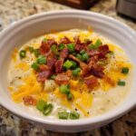 Close-up of a creamy bowl of potato soup recipe topped with bacon, cheddar cheese, and green onions.