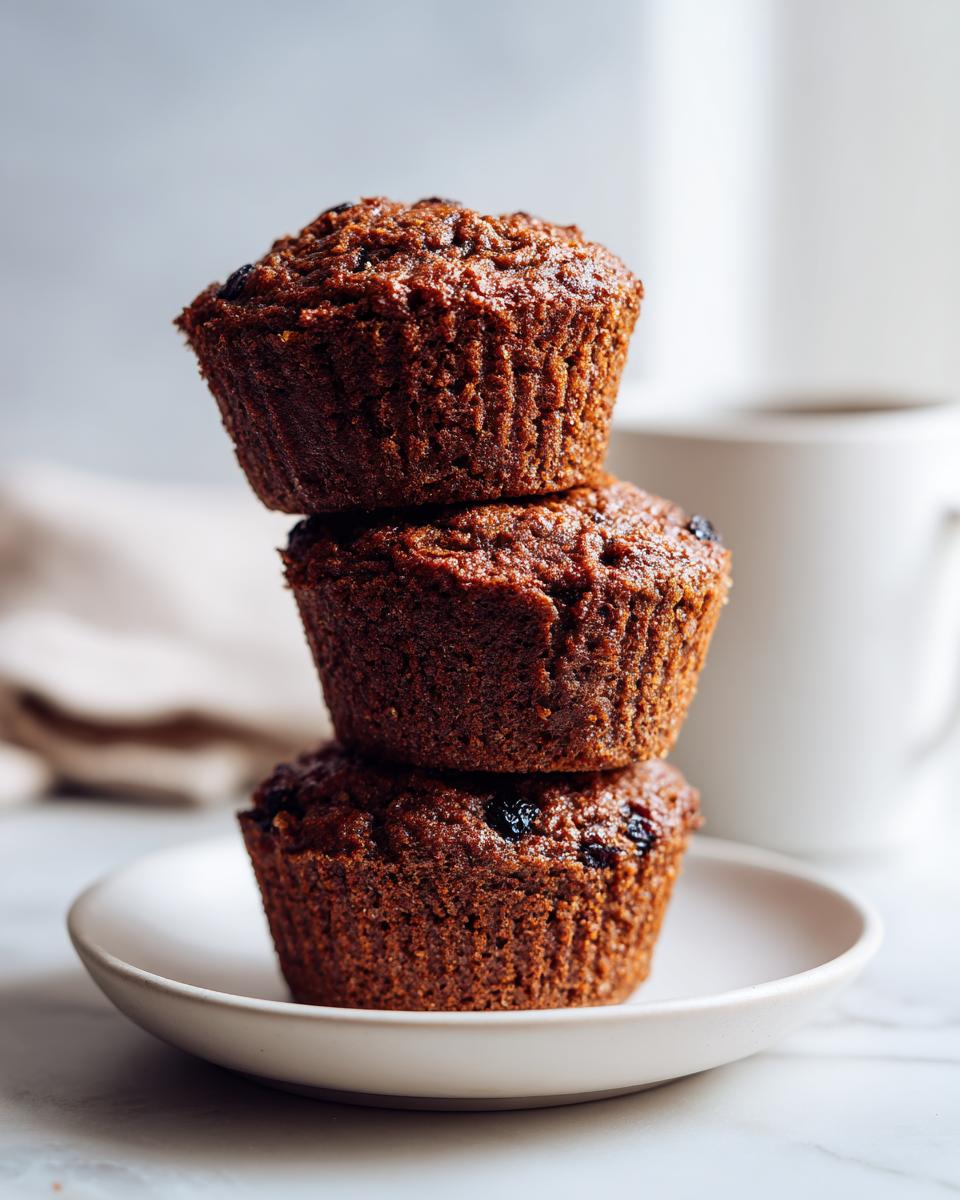 Three moist bran muffins stacked vertically on a small white plate, ready for breakfast.