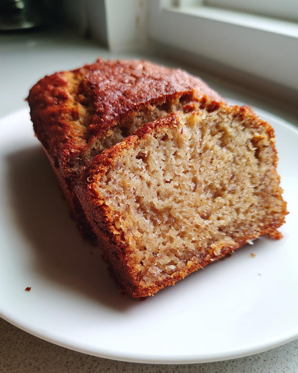 Close-up of a loaf of greek yogurt banana bread with one slice cut, showing the moist crumb texture.