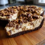 A close-up slice of creamy no-bake butterfinger pie with a chocolate crust, topped with crushed candy pieces.