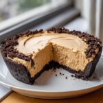 A creamy no bake peanut butter pie with a thick chocolate crust and crumb topping, one slice removed.