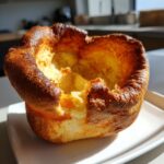 A single, perfectly risen Yorkshire pudding with a deep golden-brown, crispy edge sitting on a white plate.