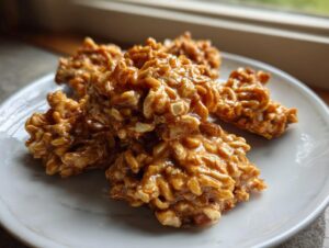 A small pile of glossy, golden-brown haystack cookies made with puffed rice cereal on a white plate.