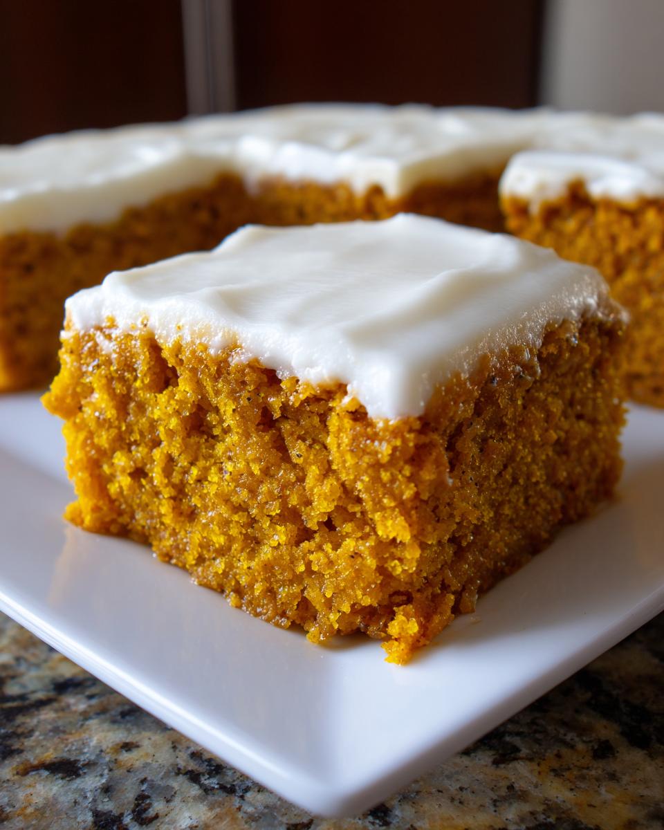 A close-up shot of a square slice of moist pumpkin bars with cream cheese frosting on a white plate.