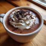Close-up of a mug filled with rich boozy hot chocolate, topped with whipped cream and dark chocolate shavings.