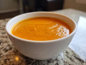 Close-up of a white bowl filled with smooth, vibrant orange roasted butternut squash soup.