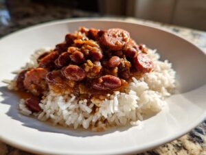 A close-up serving of amazing 1-pot red beans and rice topped with sliced smoked sausage on white rice.