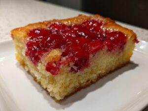 Close-up of a moist slice of cherry dump cake with a bright red, glossy cherry topping over a golden cake base.