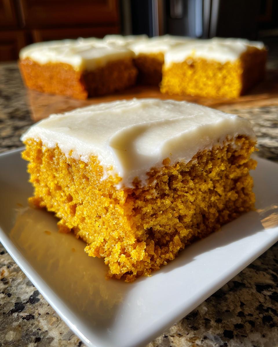 A close-up of a square slice of moist pumpkin bars with thick cream cheese frosting on a white plate.