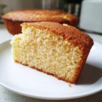 Close-up of a moist slice of vanilla cake showing its fine crumb texture on a white plate.