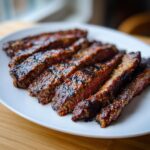 Close-up of perfectly grilled and sliced steak, glistening with the rich Carne asada marinade, served on a white plate.
