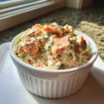A white ramekin filled with creamy smoked salmon dip, topped with chunks of salmon and fresh dill.
