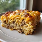 A hearty square slice of sour cream beef noodle casserole topped with melted, browned cheddar cheese.
