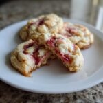 A close-up of strawberry cheesecake cookies, with one cookie broken open showing the creamy, bright red strawberry filling.