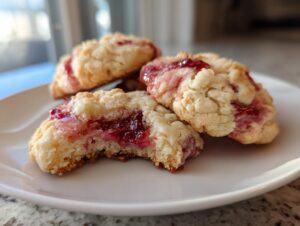 Close-up of several soft strawberry cheesecake cookies piled on a white plate, showing the gooey red filling.