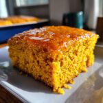 Close-up of a square slice of bright orange sweet potato cornbread topped with a shiny glaze.