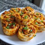 A close-up of several baked taco pinwheels arranged on a white plate, garnished with chopped green onions.