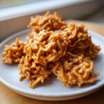 A plate of gooey, peanut butter-coated haystack cookies made with chow mein noodles.
