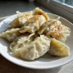 A white plate piled high with freshly cooked Traditional Chinese Dumplings, showing golden-brown sear marks.