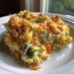 A close-up of a cheesy, golden-brown slice of vegetable casserole featuring corn, carrots, and broccoli.