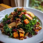 Close-up of a vibrant Fall Harvest Salad featuring kale, roasted squash, walnuts, dried cranberries, and apple slices on a white plate.