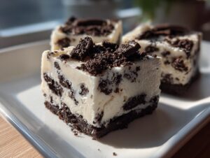 Close-up of creamy white oreo fudge squares loaded with crushed Oreo pieces, sitting on a white plate.
