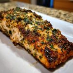 Close-up of a perfectly cooked piece of air fryer salmon with a crispy, herbed crust served on a white plate.