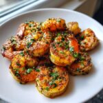 Close-up of golden brown, seasoned air fryer shrimp piled on a white plate, garnished with fresh parsley.
