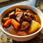 Close-up of a white bowl filled with rich, dark pork stew featuring tender chunks of meat, carrots, and potatoes.