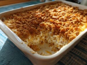 A freshly baked hot chicken salad casserole in a white dish with a golden, crunchy cornflake topping.
