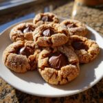 A plate of freshly baked kiss cookies, rolled in sugar and topped with a melted chocolate kiss.