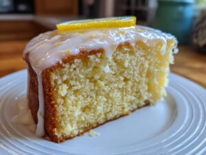Close-up of a moist slice from the amazing lemon cake recipe, topped with white glaze and a lemon slice.