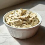 A close-up of thick, creamy olive dip seasoned with herbs in a white ramekin.