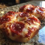 Close-up of two freshly baked pizza bagels topped with melted cheese and pepperoni slices.