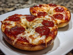 Close-up of two freshly baked pepperoni pizza bagels topped with melted mozzarella and herbs on a white plate.
