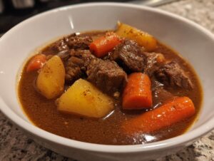 Close-up of a white bowl filled with rich, brown Amazing 8-hour pork stew chunks, potatoes, and carrots.