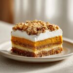 A layered slice of amazing pumpkin crunch dessert topped with whipped cream and crunchy nuts.