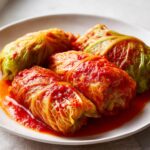 Four plump Stuffed Cabbage Rolls simmered in a rich, bright red tomato sauce, served on a white plate.