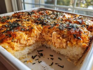 A portion of creamy baked salmon sushi bake removed from a white dish, showing layers of rice and topping.