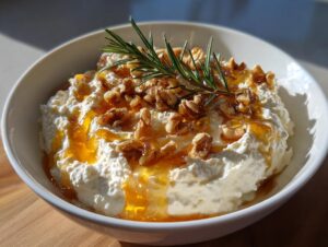 Close-up of creamy whipped ricotta dip topped with honey, chopped walnuts, and a sprig of fresh rosemary.