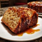 Close-up of a moist slice of apple dapple cake topped with rich caramel sauce and nuts.