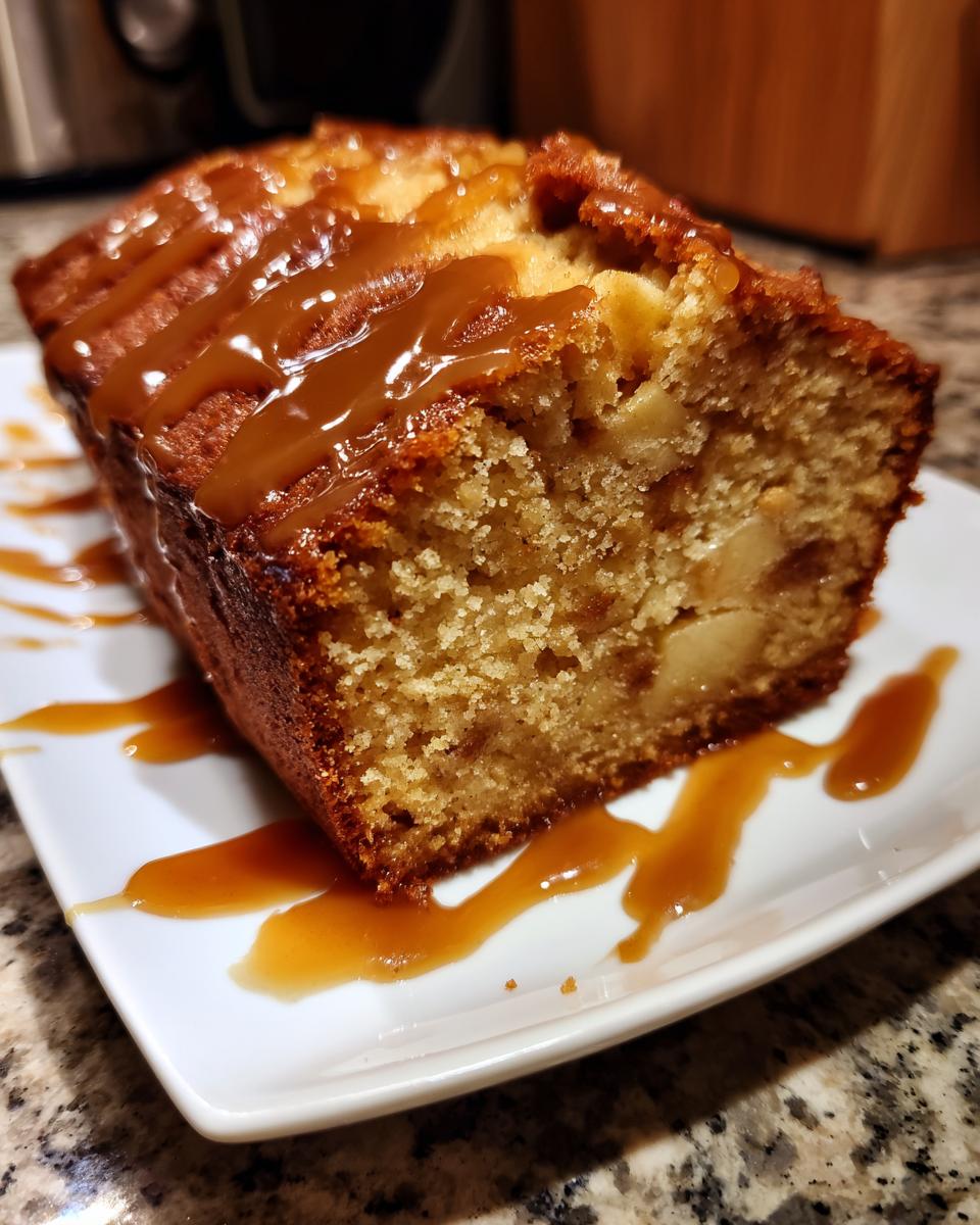 Close-up of a moist slice of apple dapple cake topped with a rich caramel drizzle on a white plate.