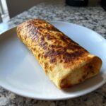 A single, perfectly baked chicken chimichanga with a golden, slightly charred tortilla served on a white plate.