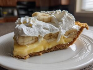 A decadent slice of banana cream pie recipe showing layers of crust, custard, banana slices, and whipped cream topping.