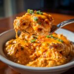 A spoonful of creamy, cheesy buffalo chicken chili topped with melted cheddar and green onions being lifted from a bowl.