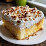 A moist slice of butter pecan praline poke cake topped with whipped cream, pecans, and caramel drizzle.