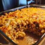 A close-up of a baked cheeseburger casserole in a glass dish, showing macaroni, ground beef, and a thick layer of melted cheddar cheese.