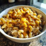 Close-up of a bowl filled with creamy homemade hamburger helper topped with melted cheddar cheese.