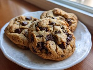Close-up of three freshly baked, chewy chocolate chip pudding cookies stacked slightly on a white plate.