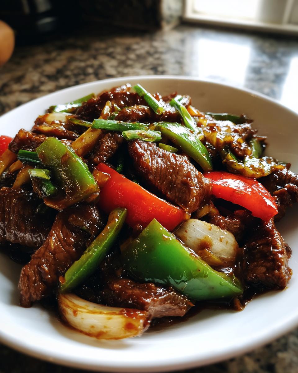 Close-up of glossy, saucy Chinese pepper steak mixed with vibrant green peppers and red bell peppers in a white bowl.
